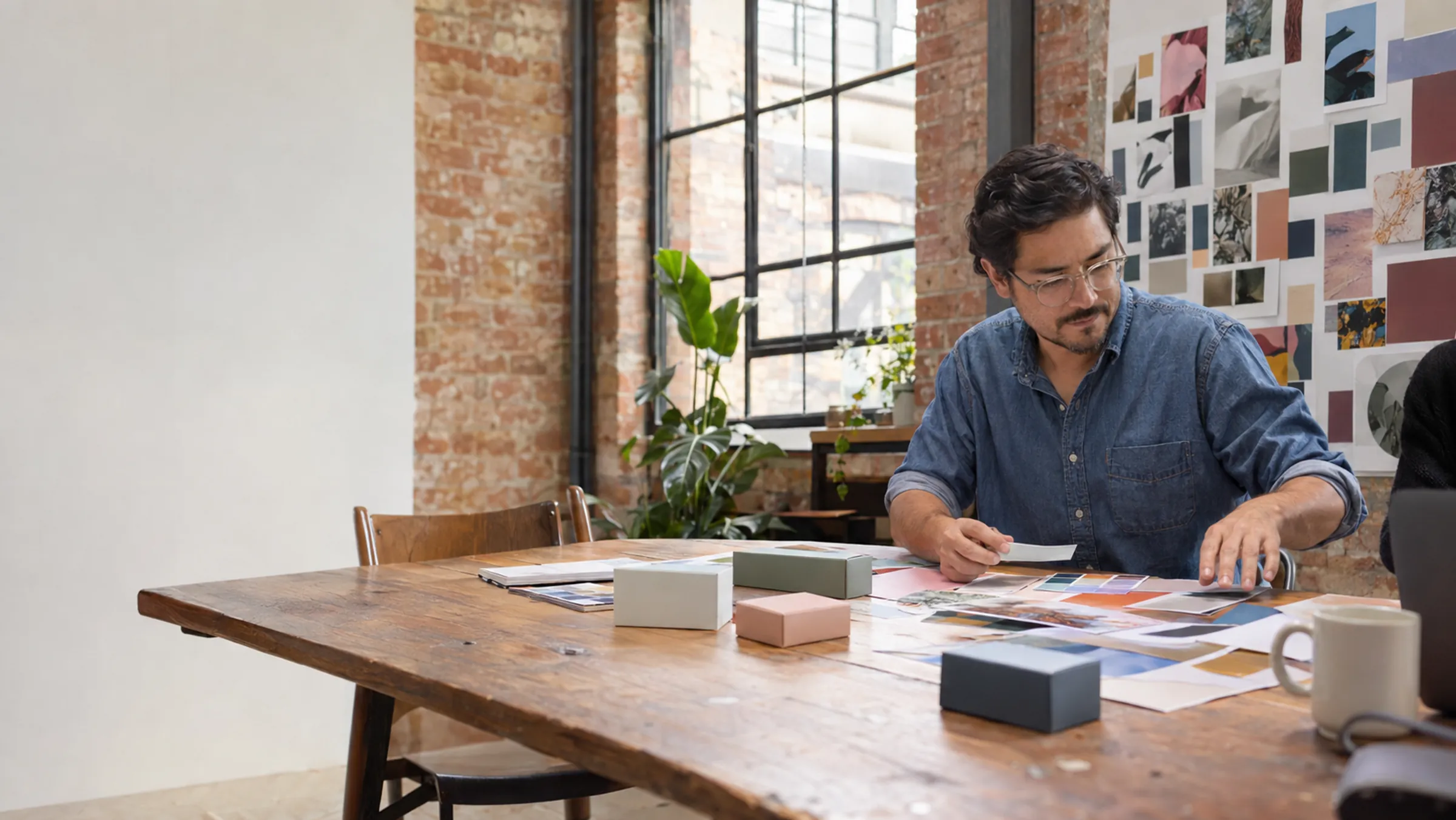 A brand designer laying out colour swatches and packaging samples in a brick-walled studio